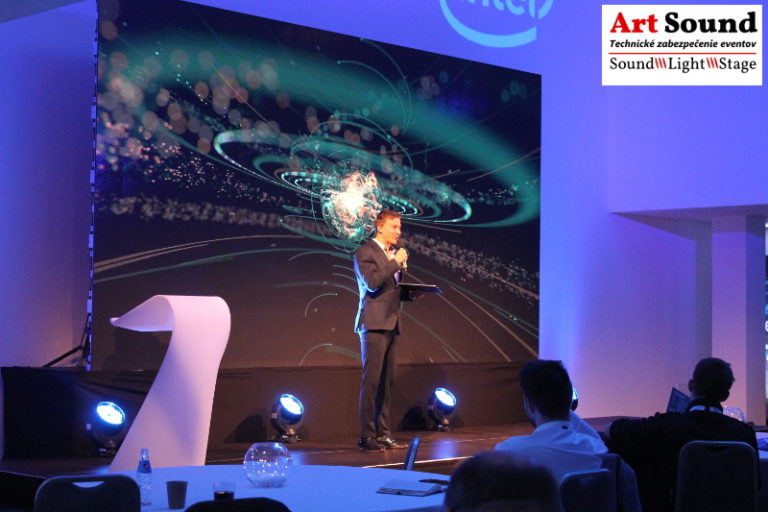 Rečník stojí na pódiu a konferenciu dopĺňa Led stena a osvetlenie.